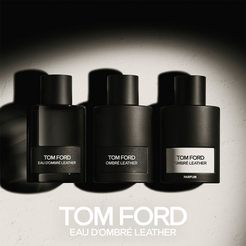 Trois flacons noirs de parfums Tom Ford alignés, étiquetés "Eau d'Ombre Leather", "Ombre Leather" et "Parfum". Ils projettent des ombres sur une surface claire, avec la mention "TOM FORD EAU D'OMBRE LEATHER" en gras en dessous.