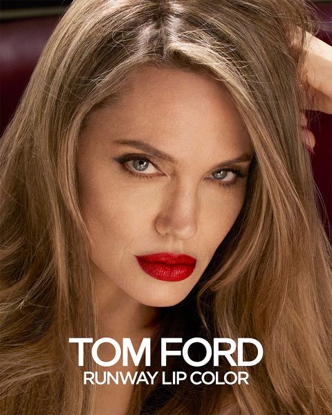 Une personne aux cheveux longs et au rouge à lèvres rouge vif fixe attentivement. L'image est une publicité pour Tom Ford Runway Lip Color, avec le nom du produit affiché en blanc en bas.