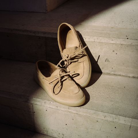 Paire de chaussures bateau beiges en daim avec lacets, reposant sur des marches en béton ensoleillées.