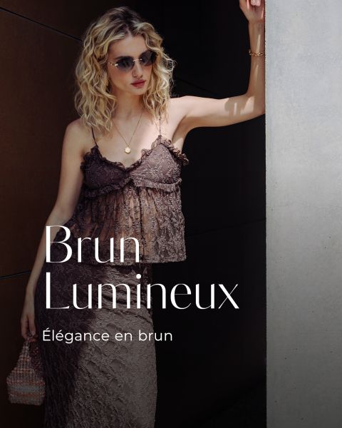 Une femme élégante avec des lunettes de soleil et une robe en dentelle marron se tient devant un mur. Texte : "Brun Lumineux, Élégance en brun."
