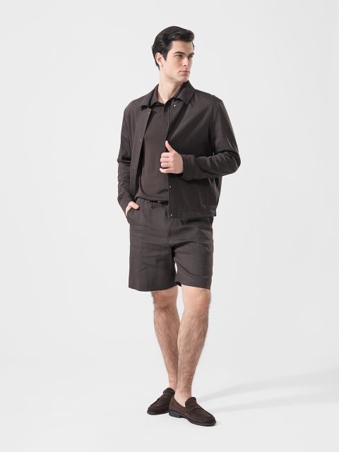 Homme en veste marron, polo assorti, short et mocassins devant un simple fond blanc.