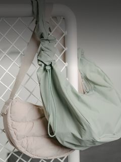 Deux sacs à bandoulière, un beige clair et un vert pâle, sont suspendus à une grille métallique blanche devant un fond neutre.