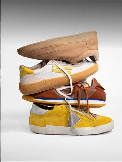 Quatre paires de baskets différentes dans les tons beige clair, blanc, marron et jaune sont empilées les unes sur les autres devant un fond uni.